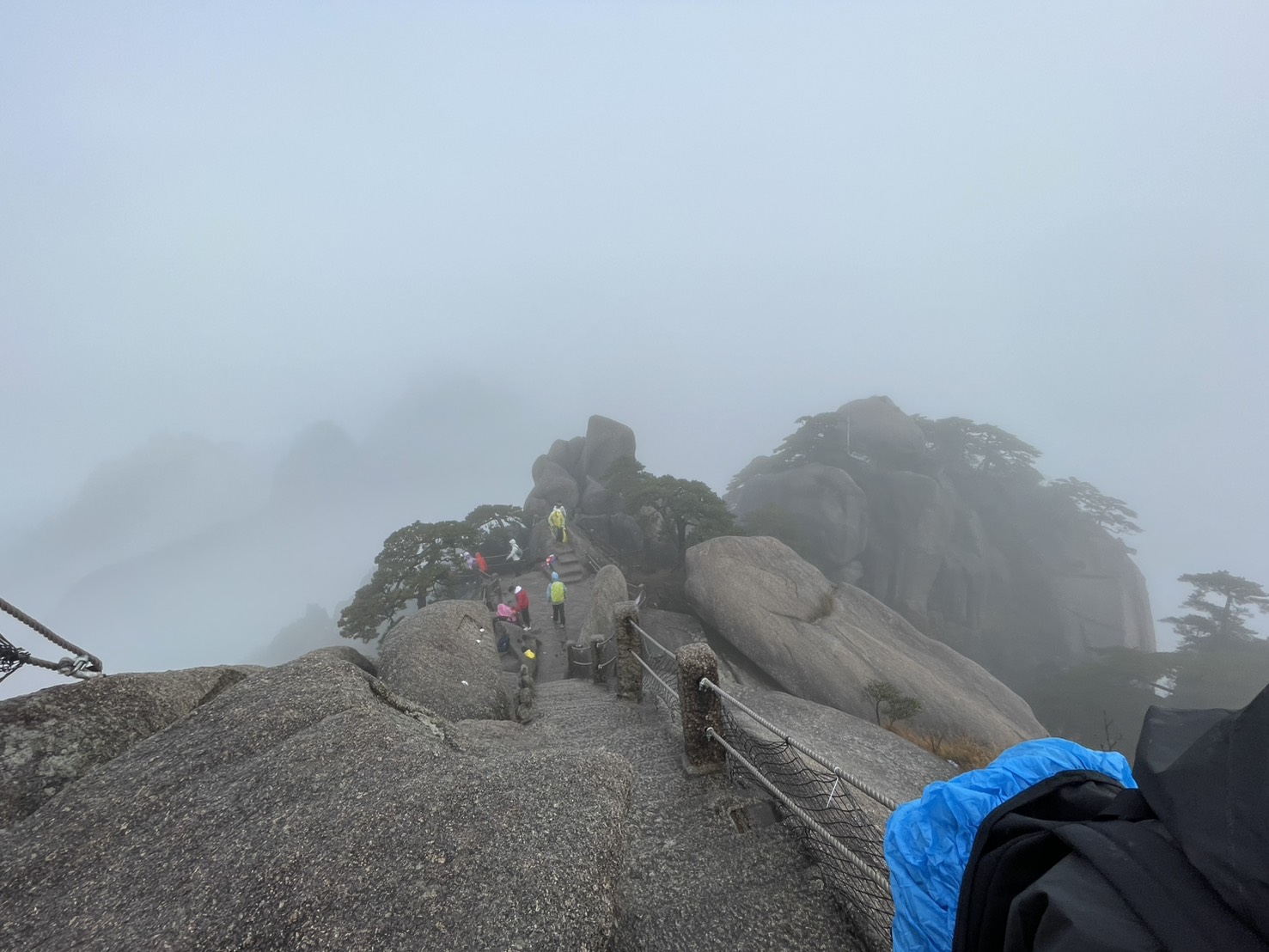霧の中、天都峰の岩場の下り道を歩くカラフルなカッパ姿の登山者たち